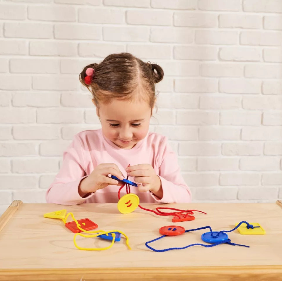 Child holding button like shapes and threading them on a red string.