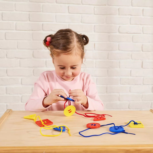 Child holding button like shapes and threading them on a red string.